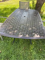 Top view of rectangular metal outdoor table with lattice design showing umbrella hole in the center, in outdoor lawn setting.