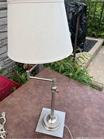 Front view of lamp showing white shade and stainless steel base on outdoor table.