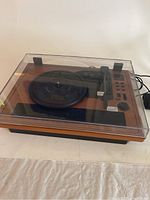 Front angled view of the Wockoder USB turntable with clear dust cover closed, showing the wood finish base and front black speaker grille