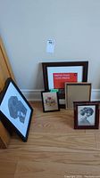 Group photo of five frames placed on floor, including prints, embroidery, and empty frames