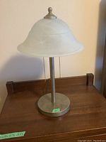 Front view of one bedside lamp showing frosted glass shade, metal base, and pull chain on wooden surface.