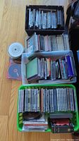 Four containers filled with assorted CDs from various artists and genres, some loose discs and cases visible