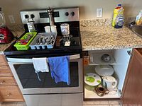 Wide view of kitchen counter showing cutlery trays with Oneida Deluxe cutlery, pepper mill, salt and pepper shakers, various kitchen utensils, and kettle on counter; cabinet open showing salad spinners, teapot without lid, and glass platter.