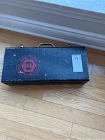 Top view of closed vintage Black & Decker black metal toolbox with red logo and text, placed on wooden floor.