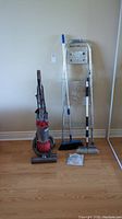 Overview of red Dyson DC25 Ball vacuum, two-step aluminum ladder, push broom, detail brush, and towel ring