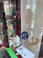 View of multiple figurines and paperweight on glass shelf showing teddy bear, rocking horse, crystal-based item and holiday figure.