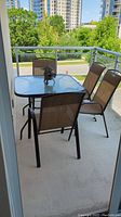 Outdoor patio set on balcony with 4 chairs surrounding square dimpled glass top table, black pagoda lantern on table