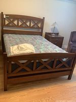 Assembled queen wooden bed frame with mattress and cover, side table and chair visible