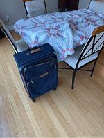 Photo of queen size Double Wedding Ring quilt draped over chairs beside upright blue suitcase.