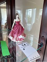 Full view of the Royal Doulton figurine displayed on glass shelf with lot tag showing 6 inches height.
