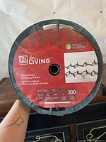 Photo of the string light reel with For Living branding, showing warm white LED label, mini bulbs spaced 3 inches apart, 300 total bulbs and 300 feet length.