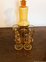 Amber glass decanter with thick stopper and four matching stemmed glasses with hand-painted gold embellishments, arranged on a wooden surface.
