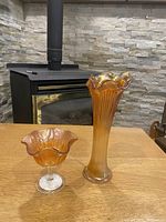 Both pieces of iridescent orange-marigold Fenton carnival glass displayed on wood table with fireplace background.