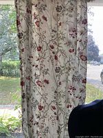 Curtain panel hung in window showing floral design and light filtering through.