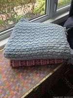 Two knit blankets folded, blue on top and pink below, showing texture and pattern.