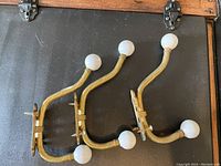Three brass hooks with white faux pearl ends laid flat for display.