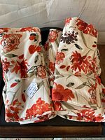Two folded stacks of floral patterned sheets and pillowcases tied with string, placed on dark wooden surface with neutral background.