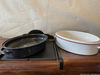 Two enamel roasting pans side by side, one black speckled and one white with red rim
