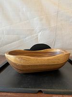 Oval two-toned wooden bowl showing side profile and thickness, placed on black tray against light background.