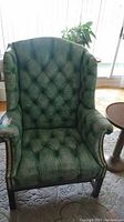 Full view of green faux leather tufted chair with high backrest, armrests, and wooden legs.