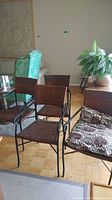 Three faux wicker chairs with metal frames showing woven seats and backs and metal armrests, placed on a wood floor with other furniture nearby.