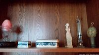 Wide view of all items arranged on a wooden shelf including pink egg, statues, trinket boxes, tall glass tube, and decorative vase-like item.