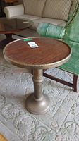 Photo of round metal end table with wood veneer top, showing decorative metal rim and base.