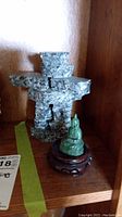 Stone Inukshuk and jade Buddha figurine on wooden shelf.