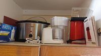 Photo showing Everstar slow cooker, Brita water pitcher box, Bon Appetit mini food processor with white base and clear bowl, Cuisinart popcorn maker in red and black color with instruction manual beside it.
