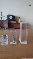 Three lucite items: one lighter with clear base and metal lighter top, one lucite paperweight with metallic sculpture inside, one tall clear lucite rectangular block paperweight.