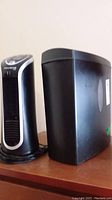 Photo showing front and side view of a black paper shredder and Rowenta Fresh Compact fan on wooden surface.