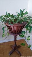 Full view of wooden plant stand holding a round flowerpot with green variegated vining plant, showing plant draping down sides.