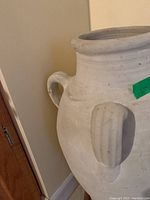 Close-up image of the top and side handles of a large off-white composite vase showing texture and minor marks.