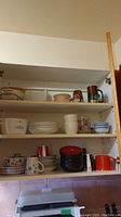 Shelf with assorted casserole dishes, bowls, mugs, and plates including CorningWare and Pyrex pieces in Blue Cornflower pattern and other colors like red and black.