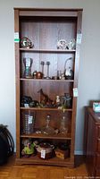 Front view of tall wooden shelving unit showing five shelves with assorted decorative items currently placed but not included with sale.