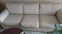 Full view of striped upholstered sofa with three seat and back cushions in beige and white vertical stripes.