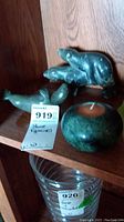 Three green stone figurines including walrus, seal, and a round candle holder with a tealight on a wooden shelf.