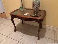 Front angled view of wooden side table with glass top and carved legs, showing scuffs on the wood surface.