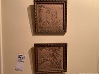 Full view of two framed cloth tapestries mounted on a wall. The frames show wear and chipping; tapestries are faded.