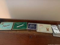 Photo showing five vintage cigarette and candy tin holders arranged side by side on a wooden surface.