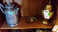 Shelf showing three items: pewter coffee pot on left, green bowl with starfish paperweight in center, brass urn on right.