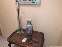 Photo showing tall clear glass vase, ceramic floral vase, and metal head decor, on a wooden side table