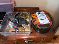 Containers holding multiple wristwatches and bands, both plastic and decorative tin.