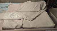Four white rectangular tablecloths folded and laid out showing different textures and embroidery.