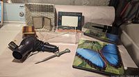 Photo showing all lot items arranged on a white surface including 2 Kleenex covers, 8 wooden coasters stacked, black travel hair dryer with coiled cord, 2 picture frames, small plastic bin, 'Costa Rica' book with butterfly cover, and wrench-shaped metal letter opener.