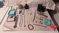 Wide shot displaying the full jewelry lot including necklaces, bracelets, earrings, decorative container, and bottle of cologne.