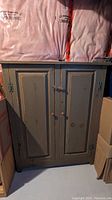 Front closed view of green rustic wooden storage cabinet with two doors, round wooden knobs, and latch.