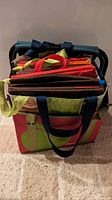Top view of multiple folded sturdy grocery bags with different colored handles stacked inside a cooler