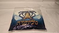 Packed prayer shawl inside clear bag with printed religious imagery and Hebrew text