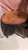 Full view of the wooden stool showing the round top surface with visible wood grain and three angled legs.
